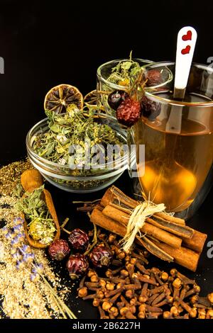 Tasse de tisanes. Divers ingrédients de tisanes dans des pots de verre sur fond noir. Médecine traditionnelle contre la grippe et le froid. Banque D'Images