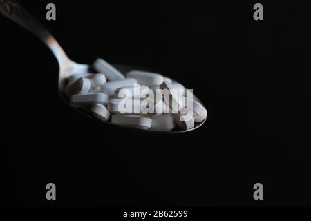 Pilules blanches déversées à partir de la cuillère comme médicament liquide avec fond noir Banque D'Images