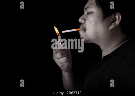 Le gros homme éclairant un joint avec le tabagisme plus léger sur le fond noir, image rapprochée de la fumée de cigarette se propagent à la main Banque D'Images