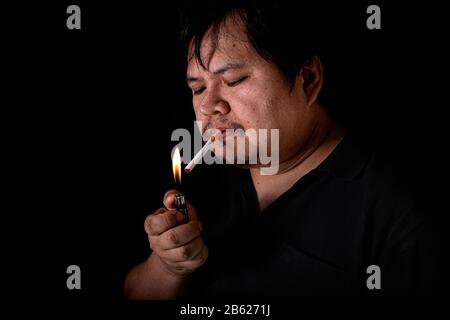 Le gros homme éclairant un joint avec le tabagisme plus léger sur le fond noir, image de la fumée de cigarette se propagent à la main Banque D'Images