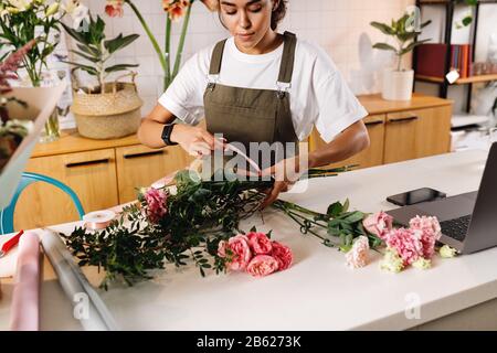 Fleuriste femme faisant un bouquet au comptoir dans un petit magasin de fleurs Banque D'Images