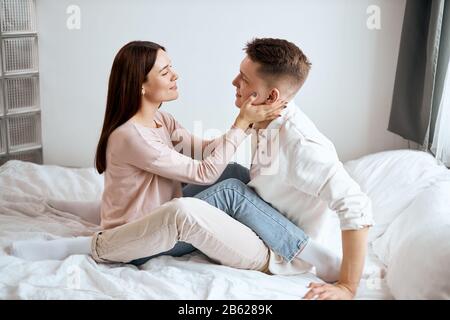 charmante fille en sweat beige et jean flirtant avec son beau petit ami portant une chemise et un pantalon blancs, photo pleine longueur. vue latérale Banque D'Images