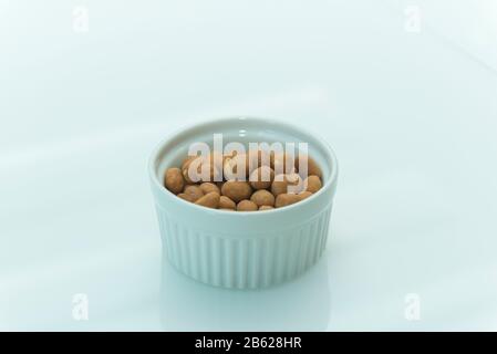 Arachides salées rôties sur fond blanc avec espace de copie. Arachides japonaises dans un bol en céramique blanc sur une table blanche. Mise au point sélective. Banque D'Images