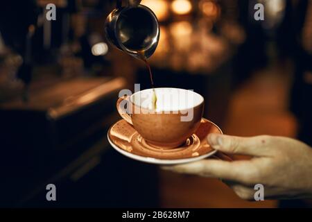 barista tenant une tasse avec du café à la source dans une tasse en acier, gros plan photo.bonjour Banque D'Images