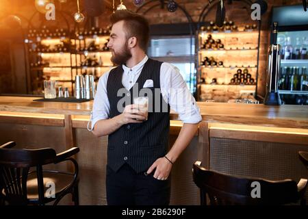 un barista souriant tenant sa main sur la poche et regardant les allées, goûter les boissons, gros plan photo Banque D'Images