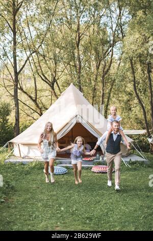 Portrait d'une femme familiale heureuse et de deux petites filles jouant à l'extérieur, tenant les mains et courir ensemble. Beau père piggybacking sa fille Banque D'Images