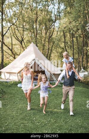 Famille caucasienne heureuse, mère de père et deux petites filles, s'amuser à l'extérieur dans le parc ou le camping, profiter du temps et rire ensemble, se tenant Banque D'Images