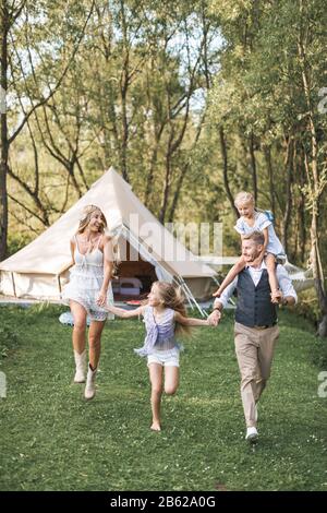 Famille caucasienne heureuse, mère de père et deux petites filles, s'amuser à l'extérieur dans le parc ou le camping, profiter du temps et rire ensemble, se tenant Banque D'Images