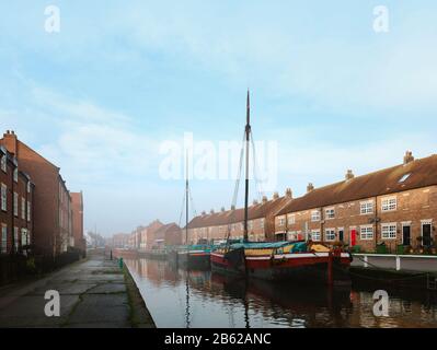 Des barges restaurés amarrés le long du beck (canal) dans un matin calme et lumineux au printemps flanqué de maisons de ville à Beverley, Yorkshire, Royaume-Uni. Banque D'Images