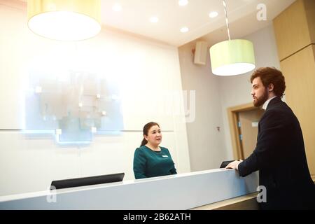 la réceptionniste a convergeant avec une photo de vue rapprochée et visiteur. la femme effectue des tâches de tenue de livres ou de caisse sur le lieu de travail. vue rapprochée v Banque D'Images