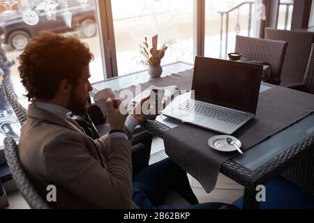 jeune homme tenant un smartphone, en sirotant du café tout en se reposer au café. gros plan sur la photo. Banque D'Images