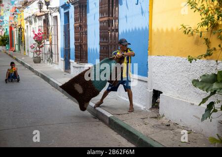 La vie continue dans cette zone touristique animée de Getsemani, homme nettoyer la poussière d'un tapis. Banque D'Images