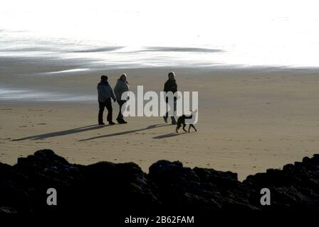 Trois personnes marchant chien sur sable, Rest Bay, Porthcawl, Glamourgan, Pays de Galles du Sud. Banque D'Images