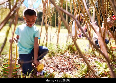 Groupe D'Enfants Portant Des Oreilles De Lapin Trouvant Des Œufs De Pâques Cachés Dans Le Jardin Banque D'Images