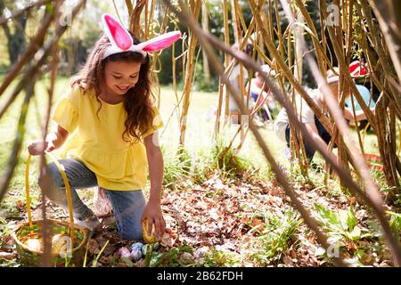 Groupe D'Enfants Portant Des Oreilles De Lapin Trouvant Des Œufs De Pâques Cachés Dans Le Jardin Banque D'Images