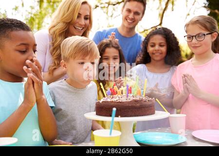 Un Garçon Souffle Sur Les Bougies LorsQu'Il Célèbre Son Anniversaire Avec La Fête Pour Ses Parents Et Ses Amis Dans Le Jardin À La Maison Banque D'Images