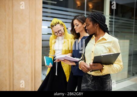 femme brunette tenant un livre, carnet, montrant ses plans, présentant son projet tout en marchant avec des collègues dans le bâtiment de bureau. gros plan Banque D'Images