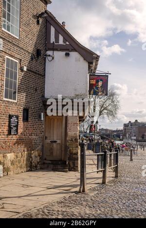 Pub Riverside à York. L'ancien bâtiment est à côté d'un chemin pavés et les clients sont assis sur des tables à l'extérieur. Un ciel nuageux est au-dessus. Banque D'Images