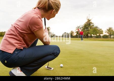 Femme Golfer Doubing Up Shot On Putting Green Comme L'Homme Tend Flag Banque D'Images