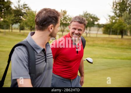 Deux Hommes D'Âge Mûr Jouant À La Ronde De Golf Portant Des Sacs De Golf Le Long De Fairway Banque D'Images