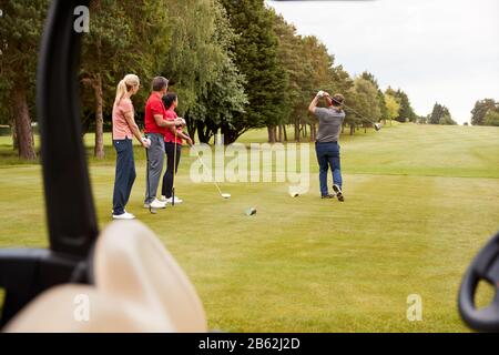 Deux Couples De Golf Se Heurtent À Tee Shot Le Long De Fairway Avec Le Chauffeur Avec Buggy À Foreground Banque D'Images