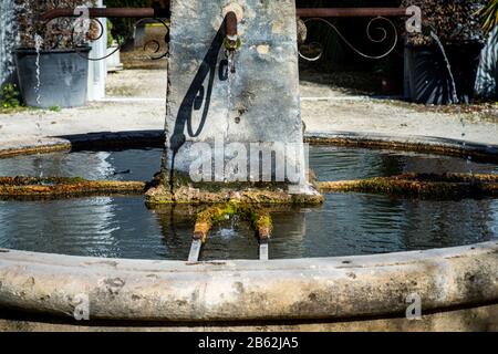 Vieille fontaine de pierre avec mousse verte et eau courante près , provence France. Banque D'Images