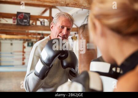 Senior Boxer Sparring Avec Entraîneur Femelle Jeune Dans La Salle De Gym Utilisant Des Gants D'Entraînement Banque D'Images