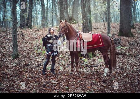 Warrior femme avec son cheval brun dans les bois - Belle fille scandinave viking - scène cinématographique médiévale Banque D'Images