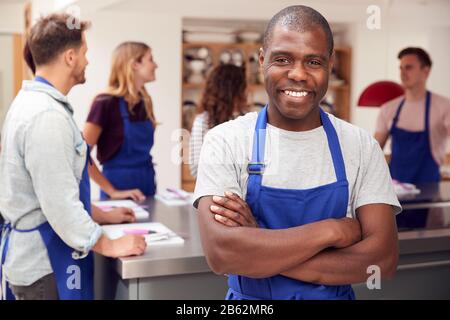 Portrait De Smiling Man Portant Un Tablier Prenant Part À La Classe Cookery Dans La Cuisine Banque D'Images