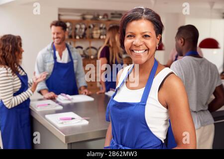 Portrait De Smiling Femme Mûre Portant Tablier Prenant Part À La Classe Cookery Dans La Cuisine Banque D'Images