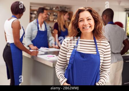 Portrait De Smiling Femme Mûre Portant Tablier Prenant Part À La Classe Cookery Dans La Cuisine Banque D'Images