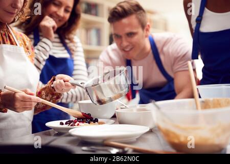 Gros Plan De La Femme Mettant Le Topping Sur Pancake En Classe Cookery Comme Les Étudiants Adultes Regardent Banque D'Images