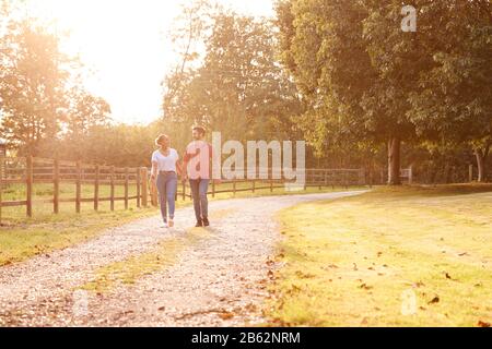Couple Romantique Marche Main Dans La Main Le Long De Country Lane Au Coucher Du Soleil Banque D'Images