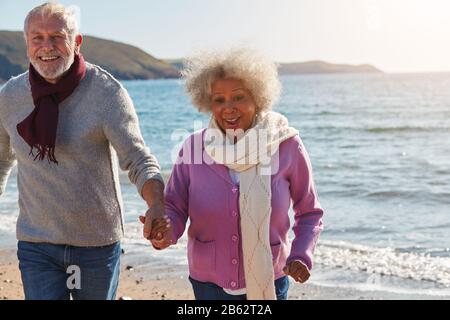Couple Senior Actif Qui Longe Winter Beach Par Waves Holding Hands Banque D'Images