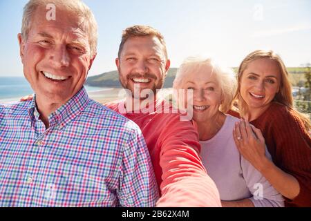 Portrait De Couple Senior Avec Progéniture Adulte Posant Pour Selfie Sur Les Vacances Au Bord De La Mer Banque D'Images
