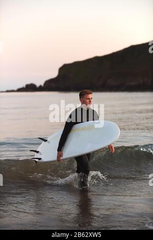 Homme Portant Des Wetsuit Transportant Surfboard LorsQu'Il Sort De La Mer