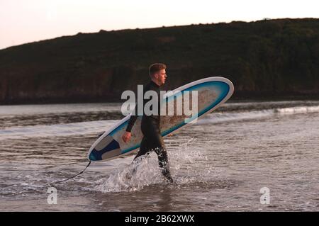 Homme Portant Des Wetsuit Transportant Surfboard LorsQu'Il Sort De La Mer