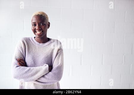 Portrait De Smiling Young Woman Debout Contre White Studio Wall Banque D'Images