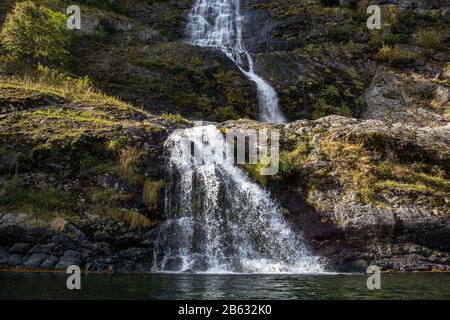 Chute d'eau tombant dans le fjord norvégien Aurlandsfjord. Vue sur l'eau blanche et vive sur la nature des montagnes sauvages de Norvège. Journée de voyage ensoleillée. Banque D'Images