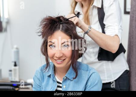 Femme coiffeur faire la coiffure en utilisant le fer à friser pour les cheveux longs de la jeune femme dans le salon de beauté Banque D'Images