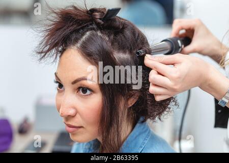 Coiffure femme coiffure rendant l'utilisation de fer à friser pour cheveux longs de jeunes femmes avec le smartphone en instituts de beauté Banque D'Images