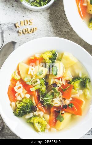 Soupe à l'alphabet pour enfants en bonne santé avec des légumes et des lettres de nouilles dans des assiettes blanches. Concept de nourriture pour bébé. Banque D'Images