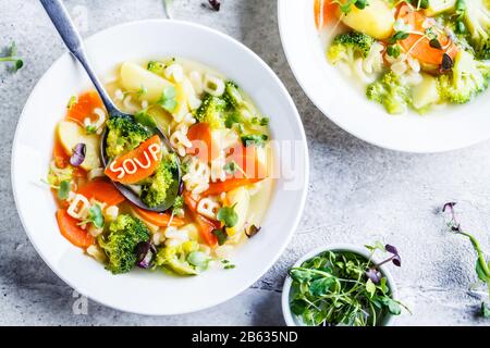 Soupe à l'alphabet pour enfants en bonne santé avec des légumes et des lettres de nouilles dans des assiettes blanches. Concept de nourriture pour bébé. Banque D'Images