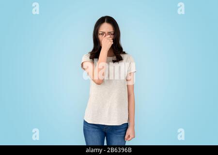 Jeune femme asiatique malsaine couvre le nez avec la main, regardant l'appareil photo, debout isolé sur fond gris avec l'espace de copie Banque D'Images