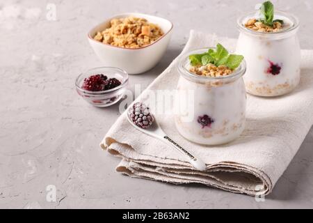 Muesli au miel croustillant de granola avec yaourt naturel, baies glacées et menthe dans des pots en verre sur fond gris, espace copie Banque D'Images