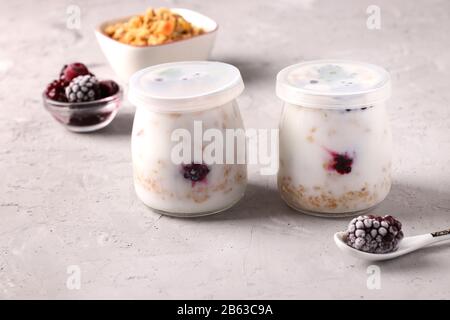 Muesli au miel croustillant de granola avec yaourt naturel et baies congelées dans des pots en verre fermés sur fond gris, nourriture saine, régime alimentaire et perte de poids Banque D'Images