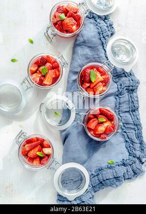 Vue en hauteur de quatre récipients en verre remplis de morceaux de fraises sur une serviette en denim. Banque D'Images