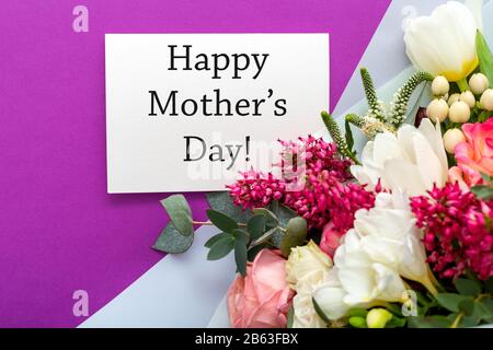 Happy Mothers Day texte sur carte cadeau avec bouquet de fleurs de roses, tulipes, eucalyptus sur fond mauve. Carte de vœux pour maman. Livraison de fleurs Banque D'Images