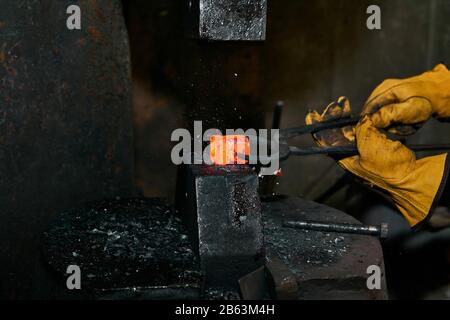 le marteau à machine rince une poêle à feu rouge tenue par un forgeron avec des pincères Banque D'Images