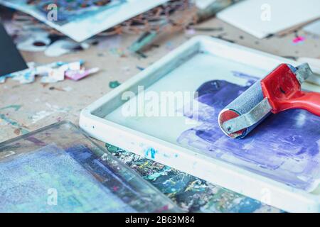 Rouleau d'encre rouge et peinture bleue éclabouillée dans le bac - des outils d'impression créatifs Banque D'Images